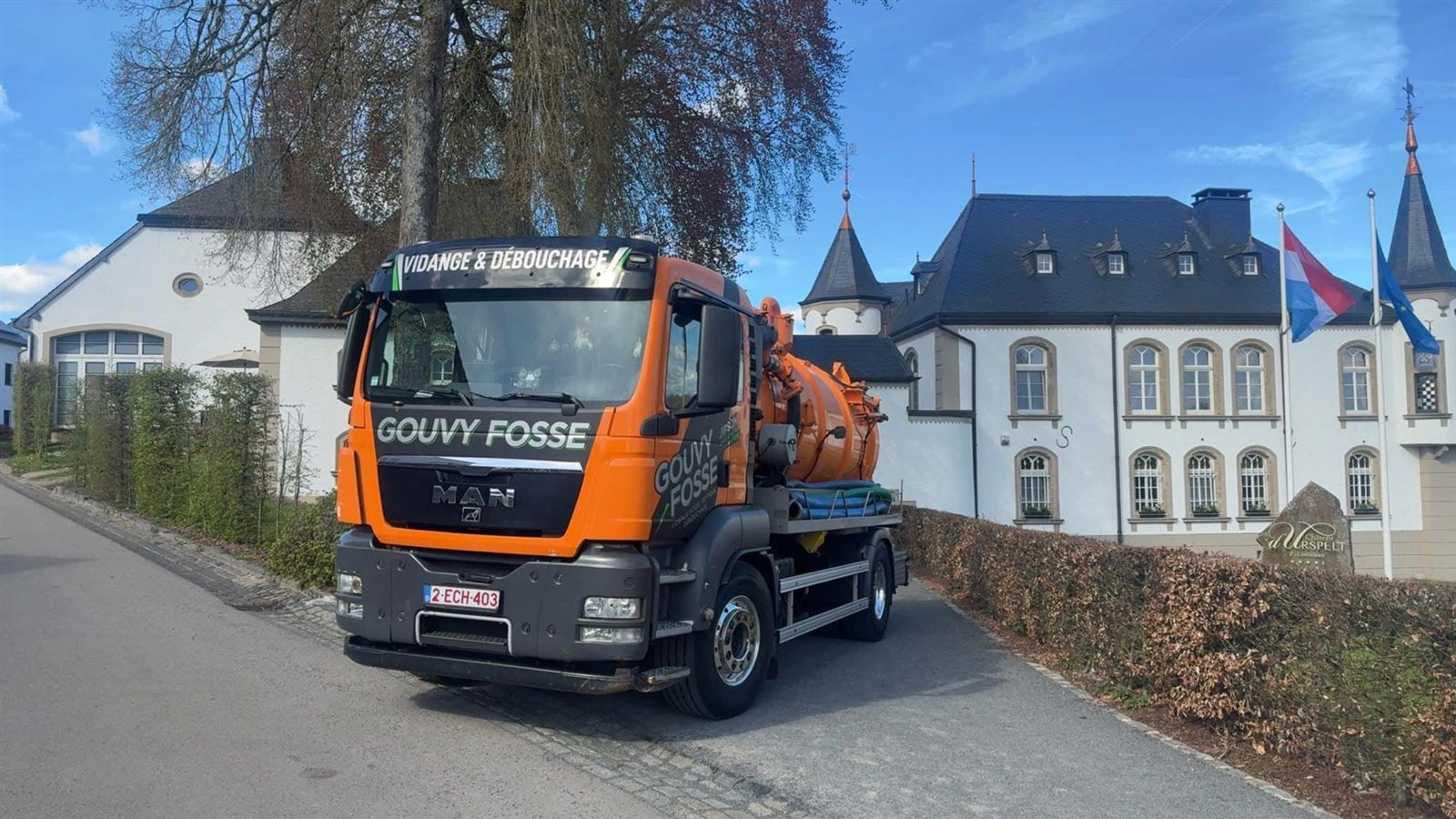 Le camion orange Gouvy Fosse devant un bâtiment en pierre